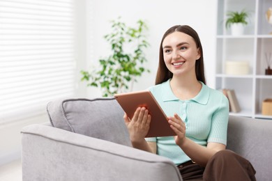 Photo of Young woman using modern tablet in armchair at home. Space for text