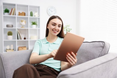 Photo of Young woman using modern tablet in armchair at home