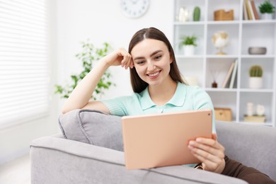 Photo of Young woman using modern tablet in armchair at home