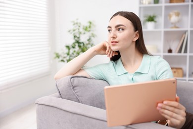 Photo of Young woman using modern tablet in armchair at home. Space for text