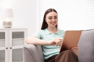Photo of Young woman using modern tablet in armchair at home. Space for text