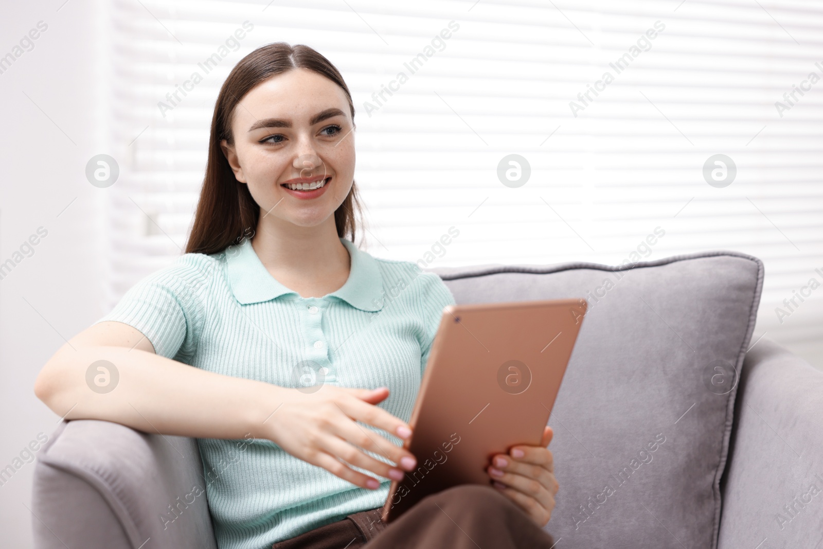 Young woman using modern tablet in armchair at home Photo of Young woman using modern tablet in armchair at home