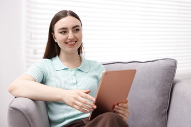 Photo of Young woman using modern tablet in armchair at home