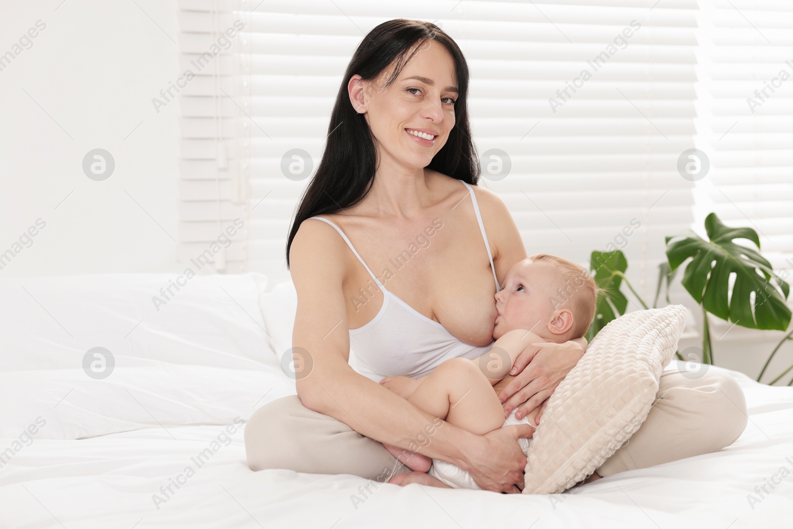 Photo of Smiling mother breastfeeding her little baby on bed indoors