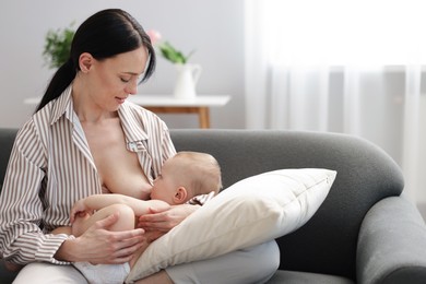Photo of Mother breastfeeding her little baby on sofa indoors