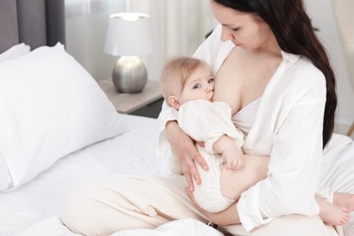 Photo of Mother breastfeeding her little baby on bed indoors