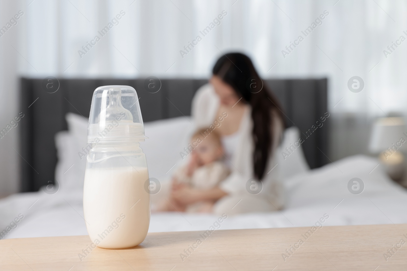 Mother with her little baby indoors, focus on bottle of milk Photo of Mother with her little baby indoors, focus on bottle of milk
