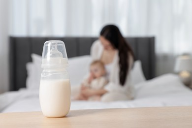Photo of Mother with her little baby indoors, focus on bottle of milk
