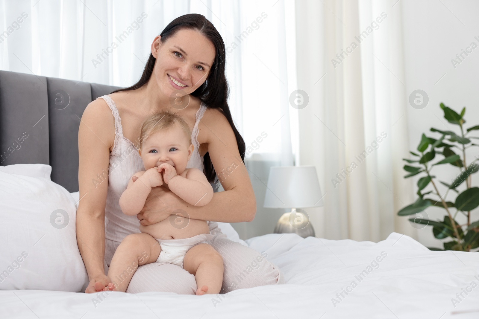 Smiling mother with her little baby on bed at home. Space for text Photo of Smiling mother with her little baby on bed at home. Space for text