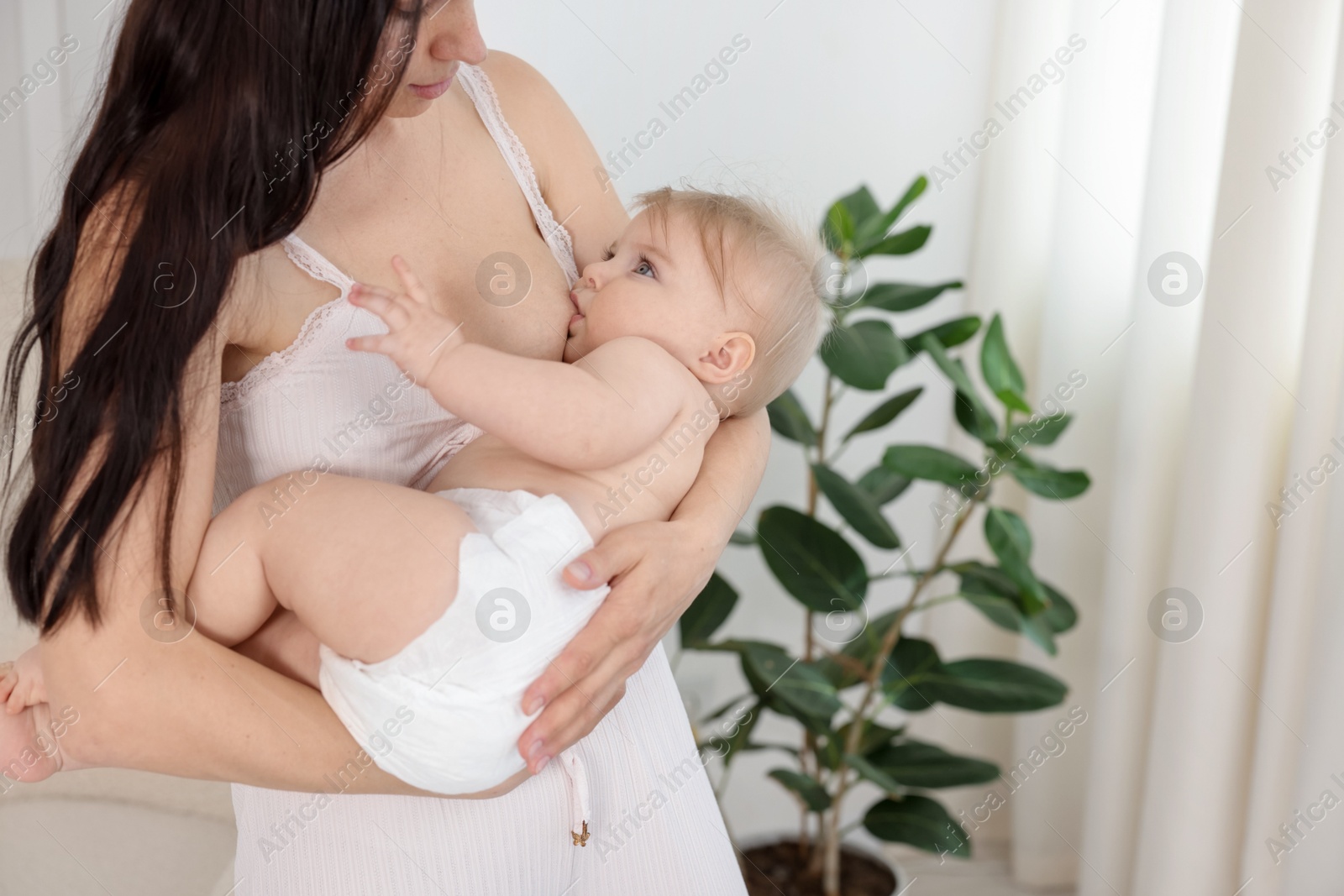 Mother breastfeeding her cute little baby indoors. Space for text Photo of Mother breastfeeding her cute little baby indoors. Space for text