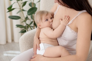 Photo of Mother breastfeeding her cute little baby on armchair indoors, closeup