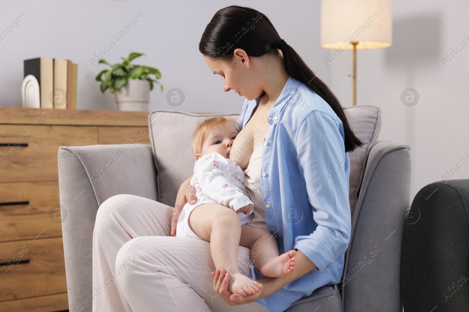 Mother breastfeeding her little baby on armchair indoors Photo of Mother breastfeeding her little baby on armchair indoors