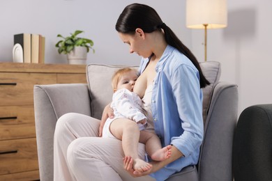 Photo of Mother breastfeeding her little baby on armchair indoors