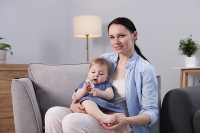 Photo of Smiling mother with her little baby on armchair indoors