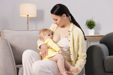 Photo of Mother breastfeeding her little baby on armchair indoors