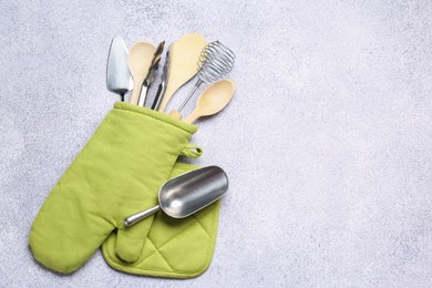 Photo of Different kitchen utensils in oven mitten on light table, top view. Space for text