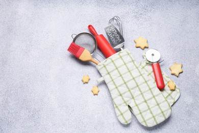 Photo of Different kitchen utensils in oven mitten and cookies on light table, flat lay. Space for text