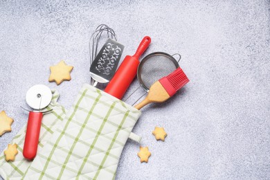 Photo of Different kitchen utensils in oven mitten and cookies on light table, flat lay