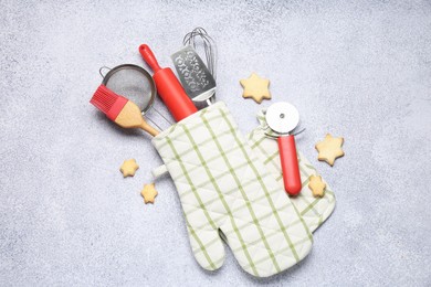 Photo of Different kitchen utensils in oven mitten and cookies on light table, flat lay