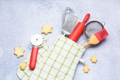 Photo of Different kitchen utensils in oven mitten and cookies on light table, flat lay