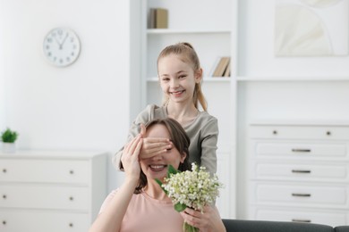 Photo of Girl giving her mother beautiful bouquet of lily-of-the-valley flowers at home