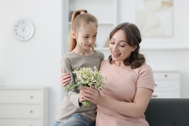 Photo of Girl giving her mother beautiful bouquet of lily-of-the-valley flowers at home