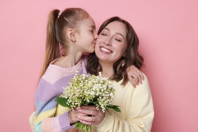 Photo of Girl kissing her mother and giving beautiful bouquet of lily-of-the-valley flowers on light pink background