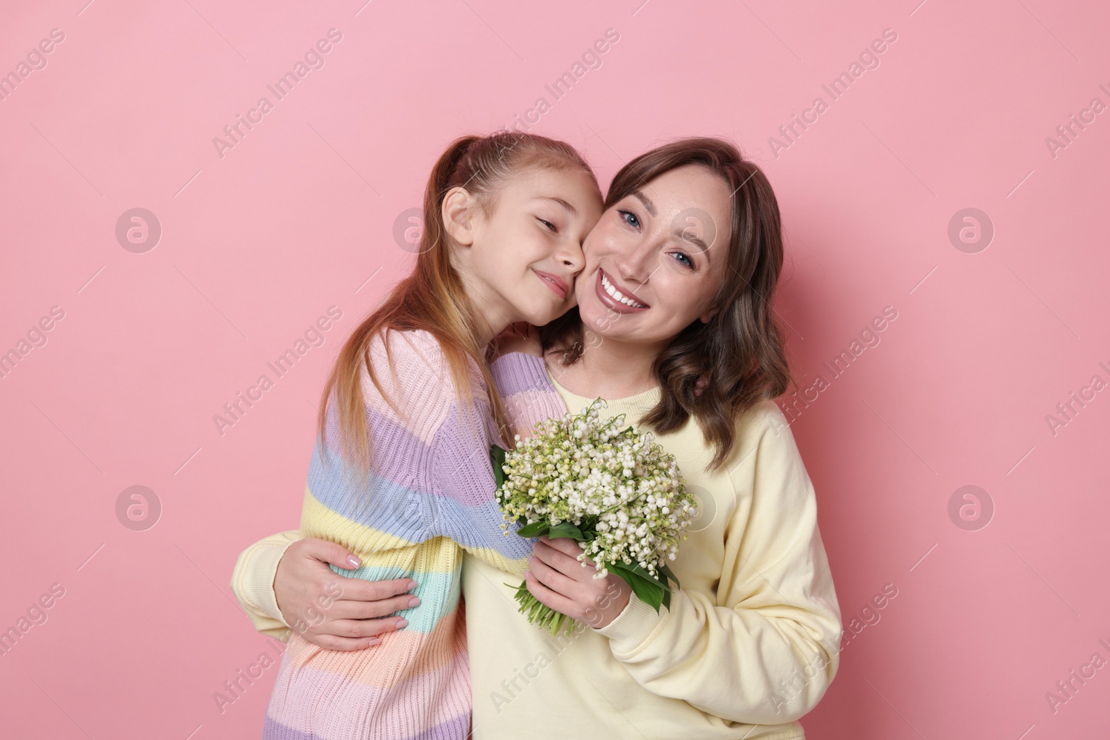 Girl giving her mother beautiful bouquet of lily-of-the-valley flowers on light pink background Photo of Girl giving her mother beautiful bouquet of lily-of-the-valley flowers on light pink background