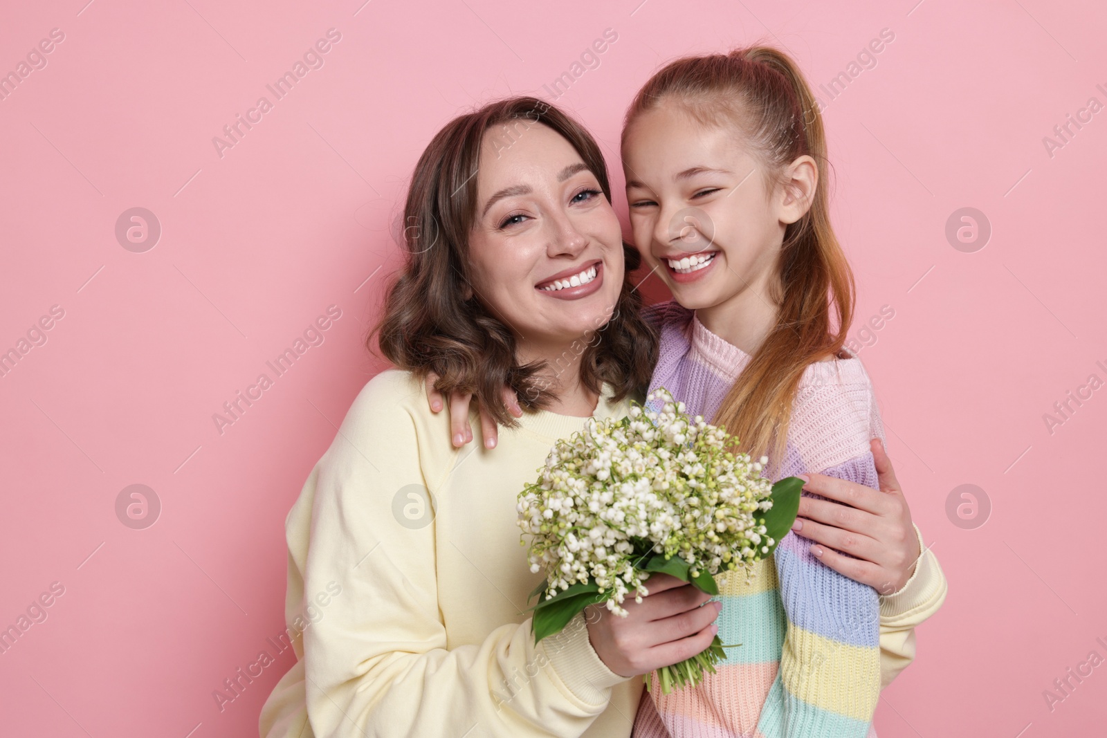 Girl giving her mother beautiful bouquet of lily-of-the-valley flowers on light pink background Photo of Girl giving her mother beautiful bouquet of lily-of-the-valley flowers on light pink background