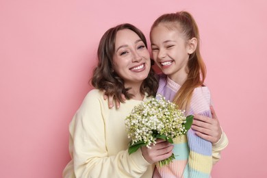 Photo of Girl giving her mother beautiful bouquet of lily-of-the-valley flowers on light pink background
