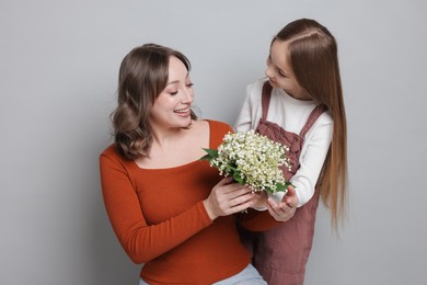 Photo of Girl giving her mom beautiful bouquet of lily-of-the-valley flowers on light grey background