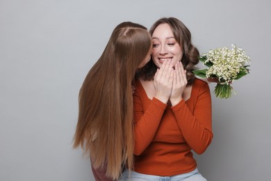 Photo of Girl giving her mom beautiful bouquet of lily-of-the-valley flowers on light grey background