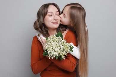 Photo of Girl kissing her mom and giving beautiful bouquet of lily-of-the-valley flowers on light grey background