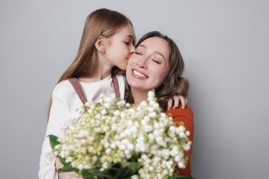 Photo of Girl kissing her mom and giving beautiful bouquet of lily-of-the-valley flowers on light grey background