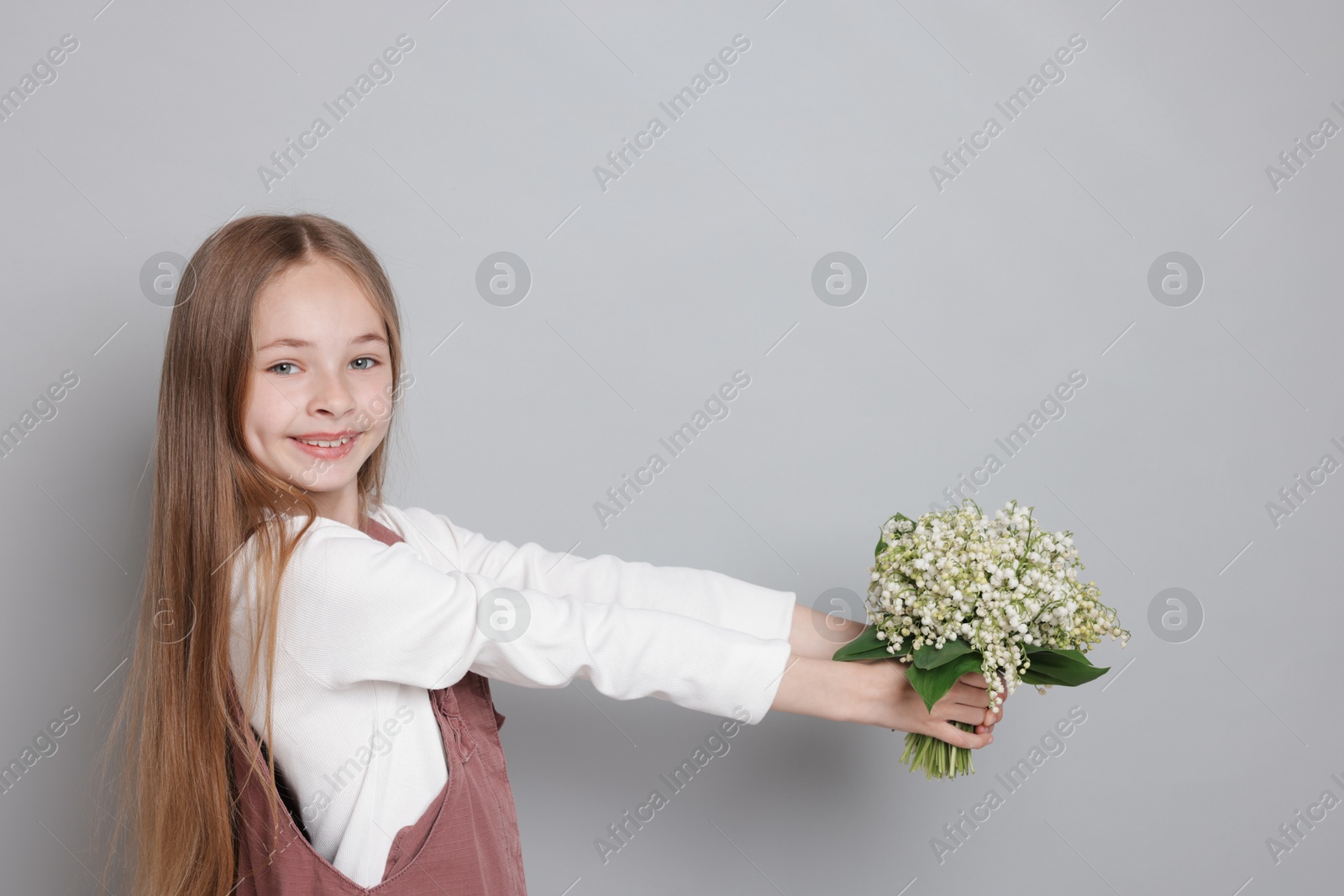 Girl with bouquet of beautiful lily-of-the-valley flowers on light grey background. Space for text Photo of Girl with bouquet of beautiful lily-of-the-valley flowers on light grey background. Space for text
