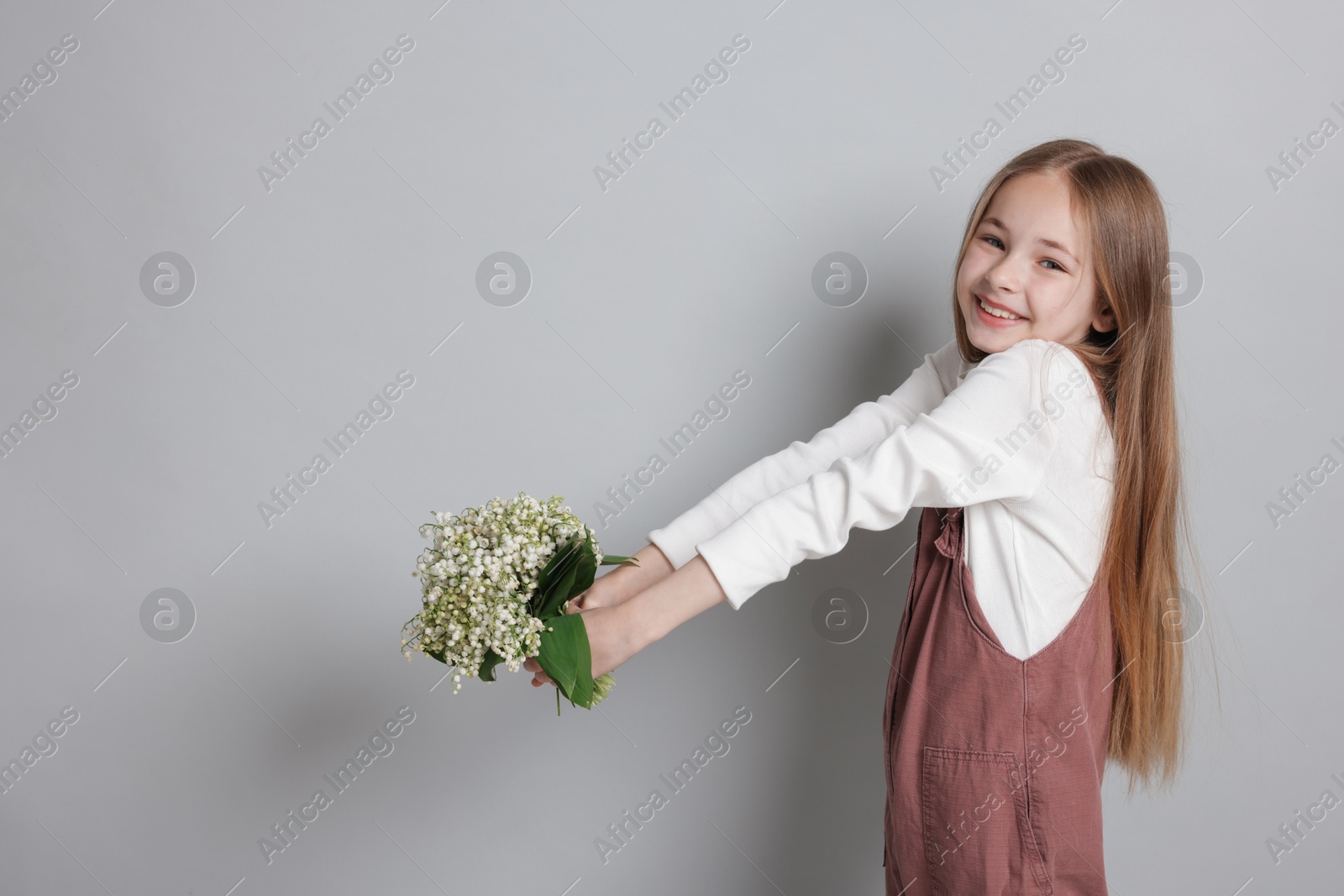 Girl with bouquet of beautiful lily-of-the-valley flowers on light grey background. Space for text Photo of Girl with bouquet of beautiful lily-of-the-valley flowers on light grey background. Space for text