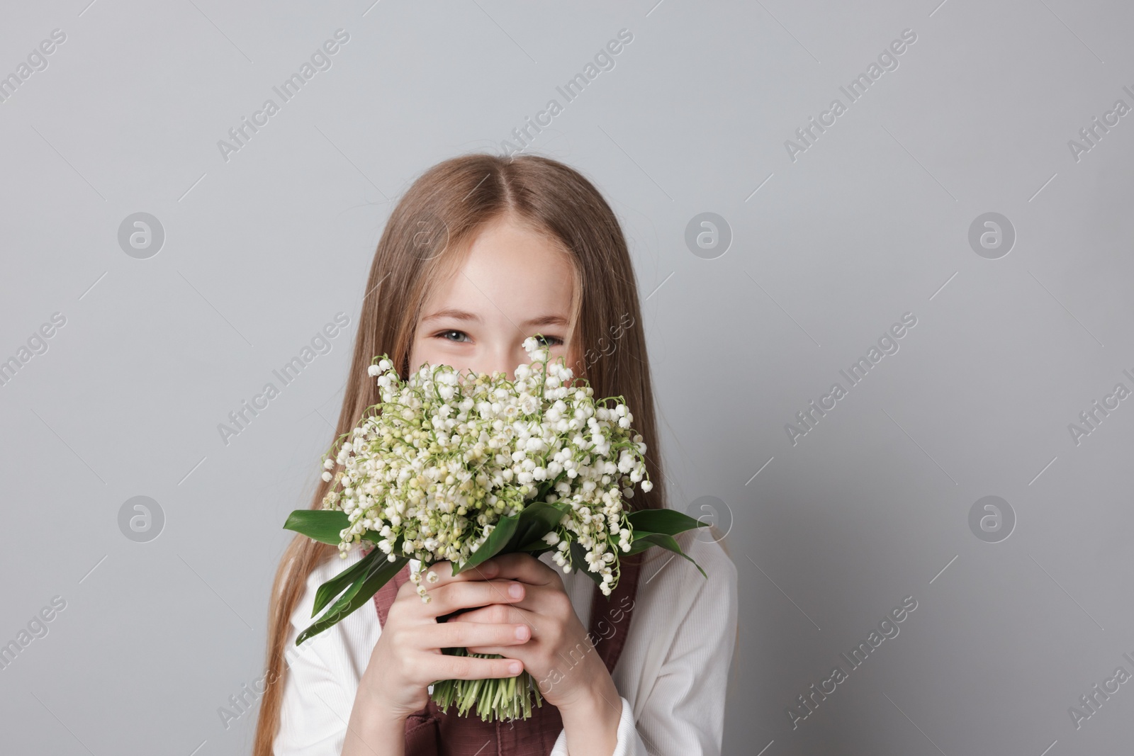 Girl with bouquet of beautiful lily-of-the-valley flowers on light grey background Photo of Girl with bouquet of beautiful lily-of-the-valley flowers on light grey background