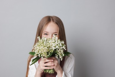 Photo of Girl with bouquet of beautiful lily-of-the-valley flowers on light grey background