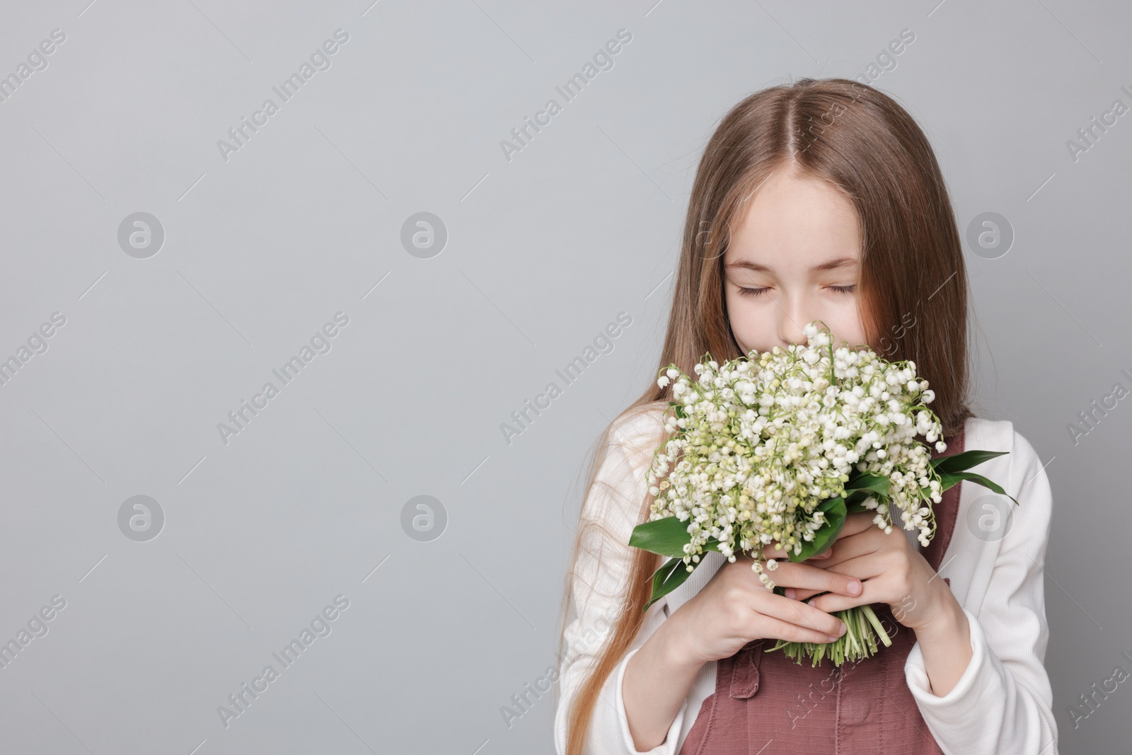 Girl with bouquet of beautiful lily-of-the-valley flowers on light grey background. Space for text Photo of Girl with bouquet of beautiful lily-of-the-valley flowers on light grey background. Space for text