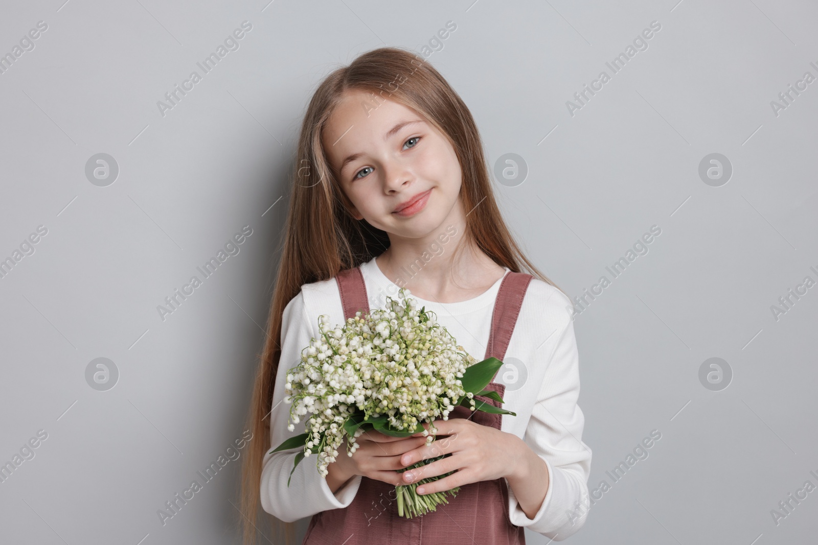 Girl with bouquet of beautiful lily-of-the-valley flowers on light grey background Photo of Girl with bouquet of beautiful lily-of-the-valley flowers on light grey background