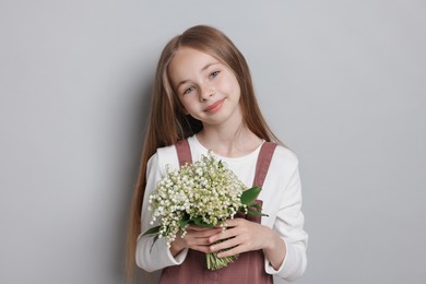 Photo of Girl with bouquet of beautiful lily-of-the-valley flowers on light grey background