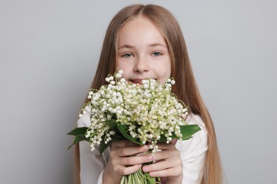 Photo of Girl with bouquet of beautiful lily-of-the-valley flowers on light grey background