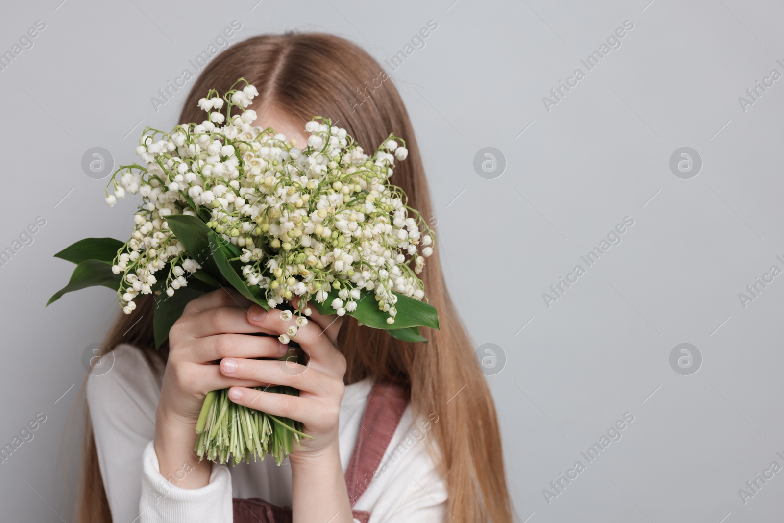 Girl with bouquet of beautiful lily-of-the-valley flowers on light grey background Photo of Girl with bouquet of beautiful lily-of-the-valley flowers on light grey background