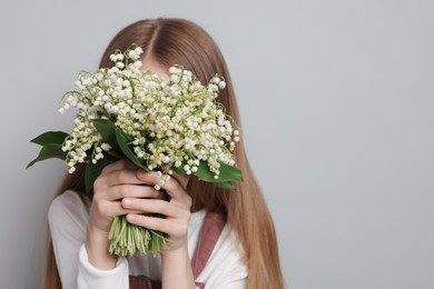 Photo of Girl with bouquet of beautiful lily-of-the-valley flowers on light grey background