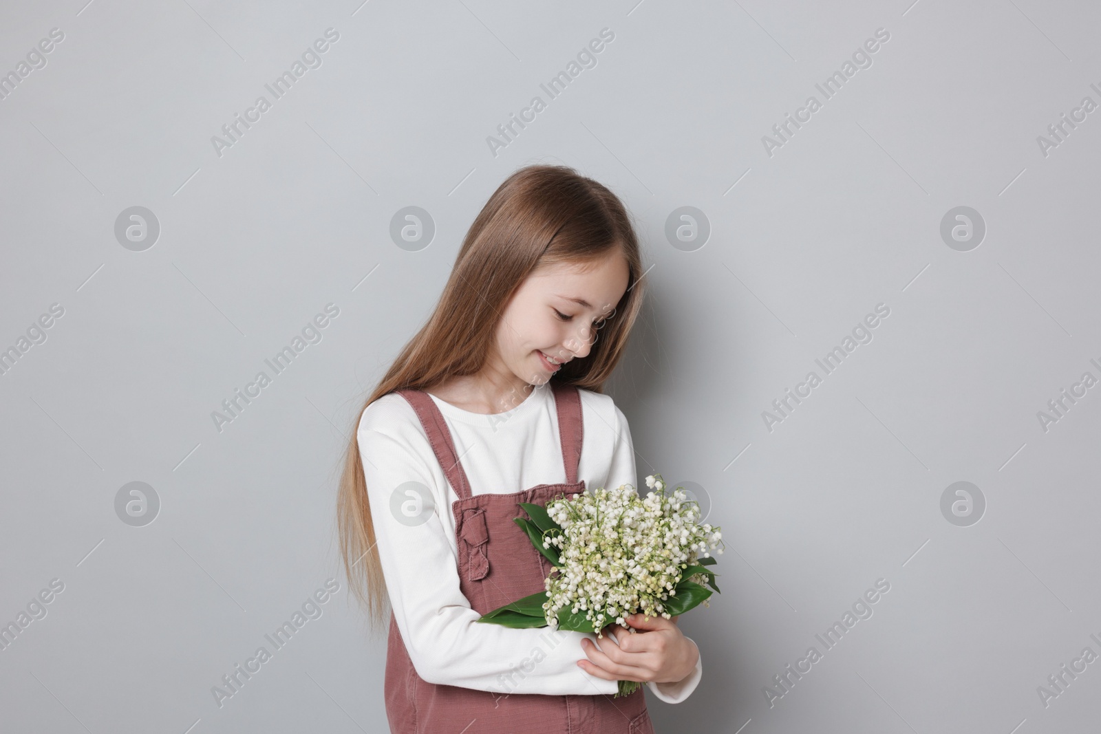 Girl with bouquet of beautiful lily-of-the-valley flowers on light grey background Photo of Girl with bouquet of beautiful lily-of-the-valley flowers on light grey background