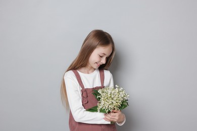Photo of Girl with bouquet of beautiful lily-of-the-valley flowers on light grey background
