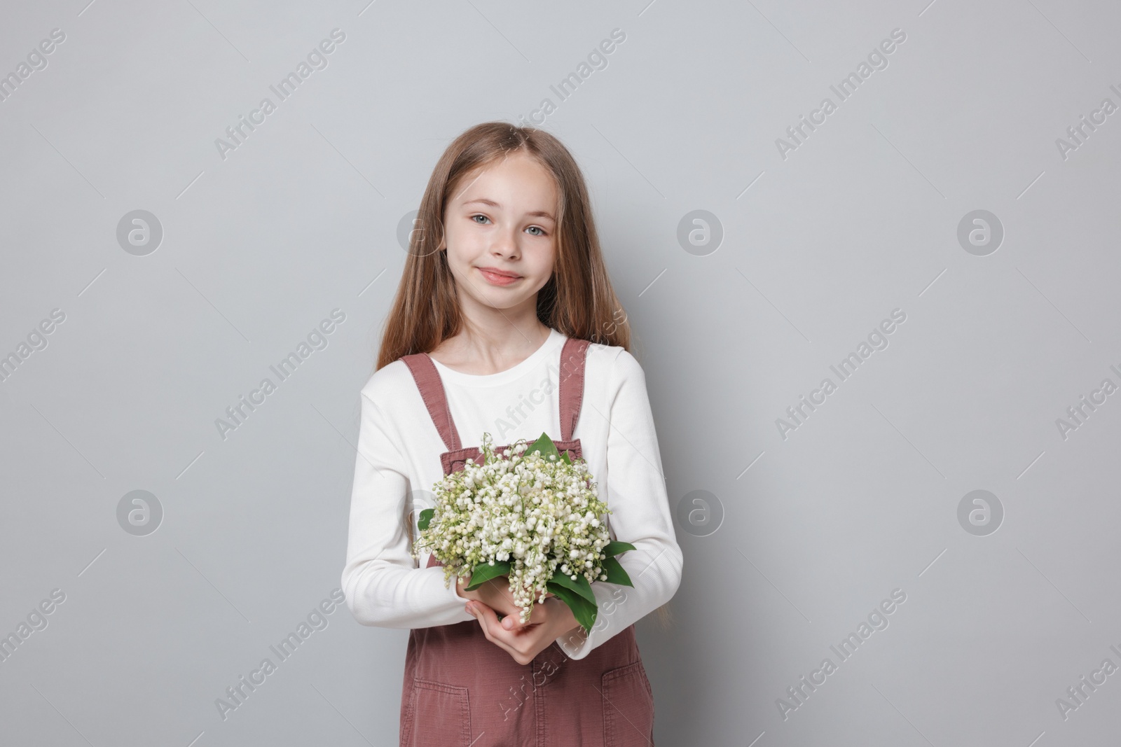 Girl with bouquet of beautiful lily-of-the-valley flowers on light grey background Photo of Girl with bouquet of beautiful lily-of-the-valley flowers on light grey background