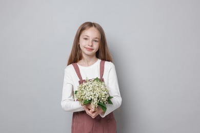 Photo of Girl with bouquet of beautiful lily-of-the-valley flowers on light grey background