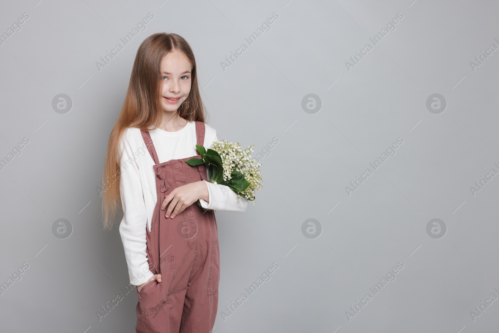 Girl with bouquet of beautiful lily-of-the-valley flowers on light grey background. Space for text Photo of Girl with bouquet of beautiful lily-of-the-valley flowers on light grey background. Space for text