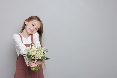 Photo of Girl with bouquet of beautiful lily-of-the-valley flowers on light grey background. Space for text